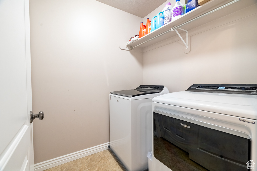Clothes washing area with washer and clothes dryer, laundry area, tile patterned flooring, and baseboards