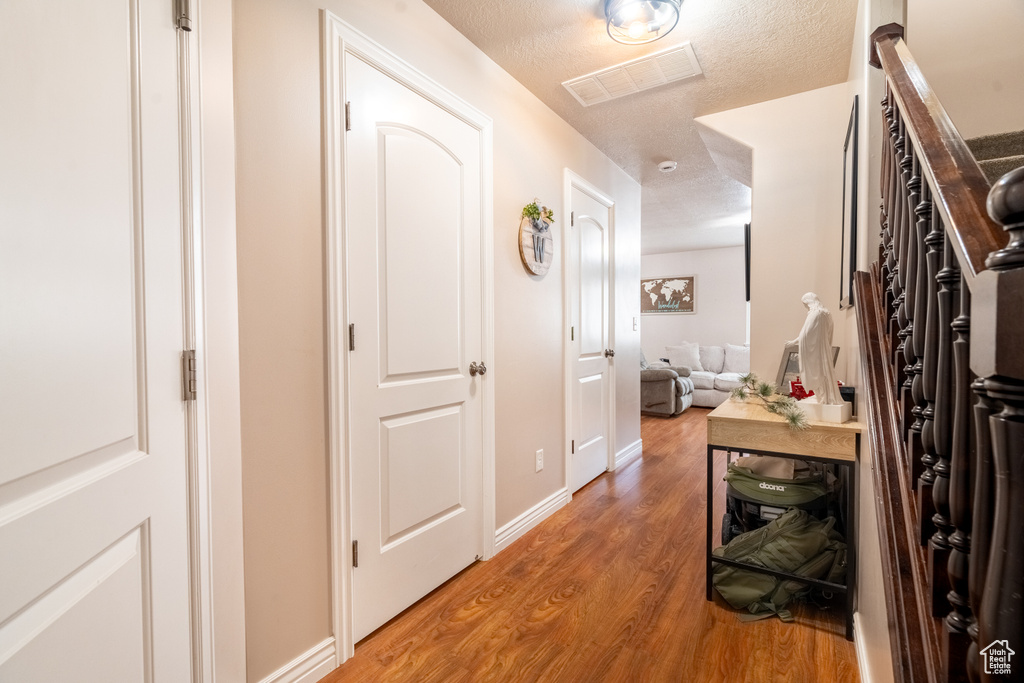 Hallway featuring visible vents, light wood-style flooring, a textured ceiling, and baseboards