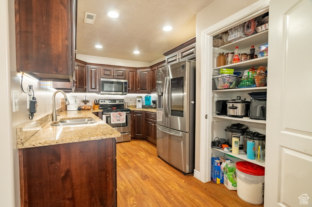 Kitchen featuring light stone counters, a sink, stainless steel appliances, dark brown cabinets, and light wood-style floors