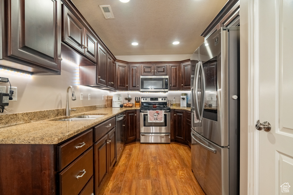 Kitchen featuring visible vents, dark brown cabinetry, light wood-type flooring, appliances with stainless steel finishes, and a sink