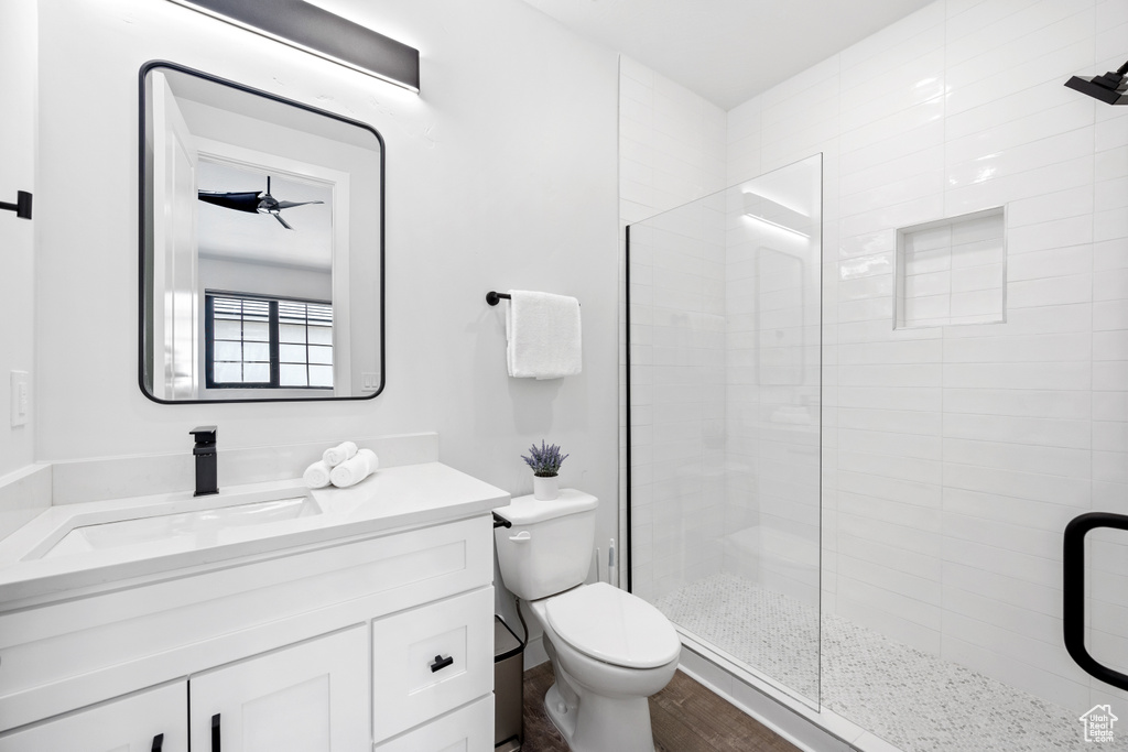 Bathroom featuring toilet, a shower with shower door, ceiling fan, wood-type flooring, and vanity