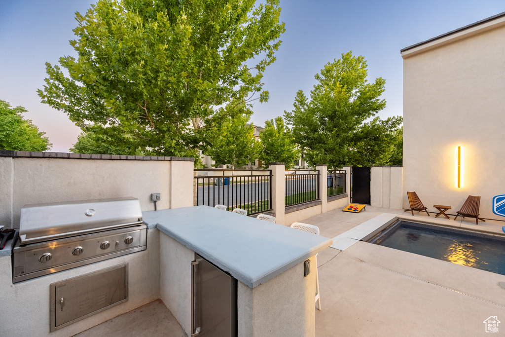 Patio terrace at dusk with grilling area, a fenced in pool, and area for grilling