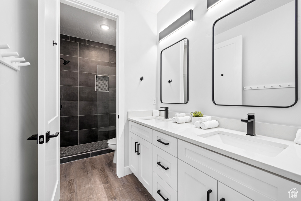 Bathroom with toilet, tiled shower, hardwood / wood-style flooring, and vanity