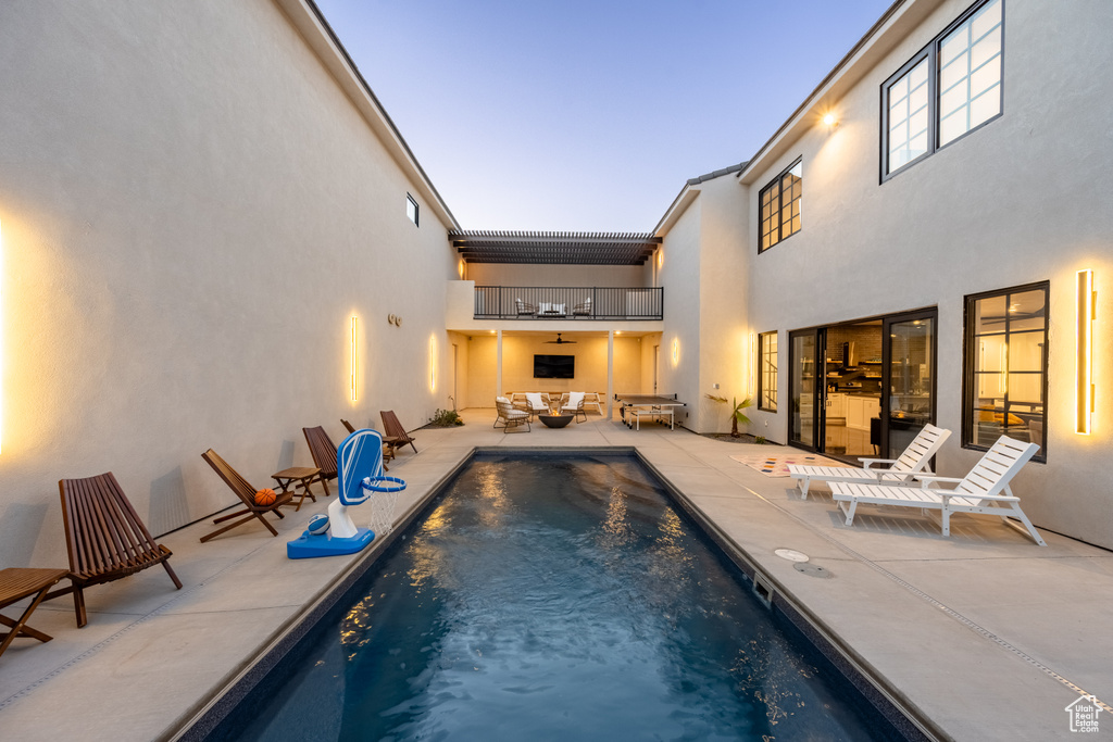 Pool at dusk with an outdoor hangout area, ceiling fan, and a patio