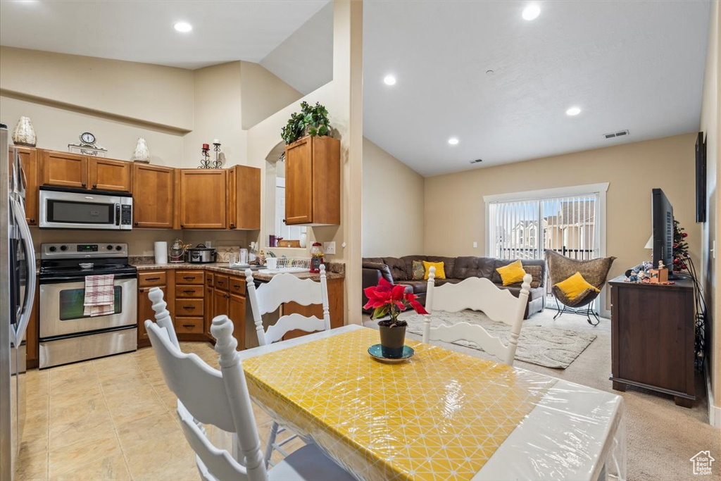 Kitchen with appliances with stainless steel finishes, light colored carpet, and lofted ceiling