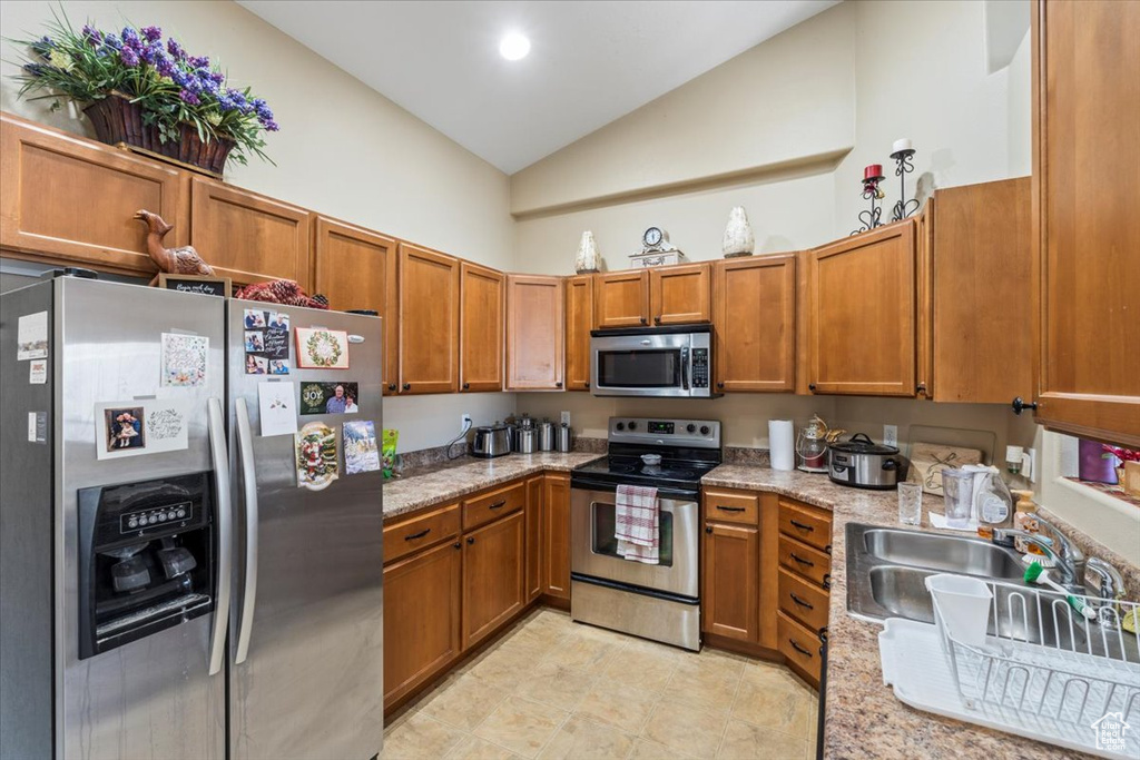 Kitchen featuring sink, stainless steel appliances, vaulted ceiling, and light stone countertops