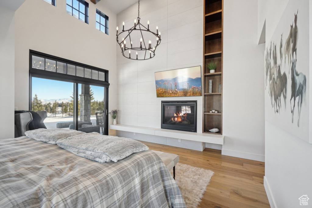 Bedroom featuring a towering ceiling, a chandelier, baseboards, wood finished floors, and a tile fireplace