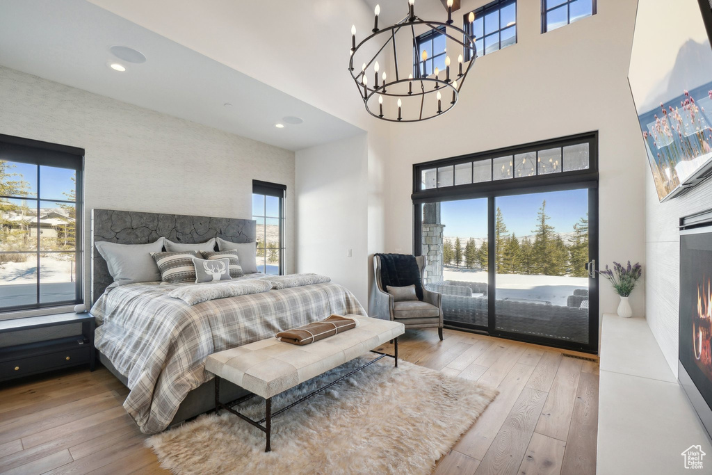 Bedroom featuring access to outside, hardwood / wood-style flooring, multiple windows, a high ceiling, and a chandelier