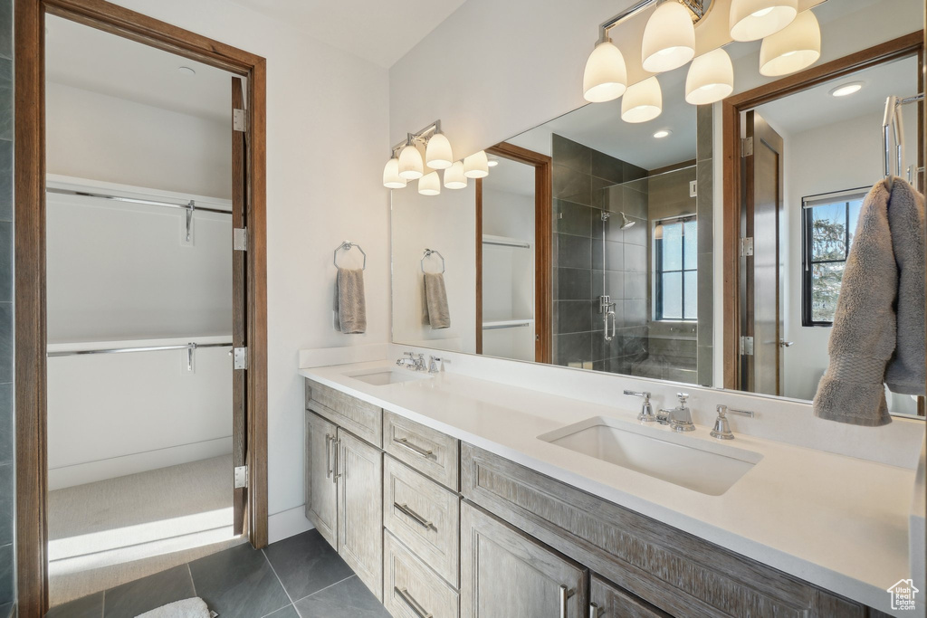 Full bath with double vanity, a tile shower, and a walk in closet