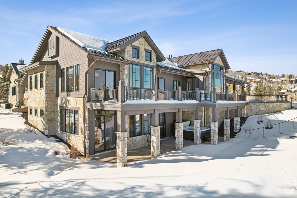 Snow covered property featuring stone siding, a standing seam roof, and metal roof