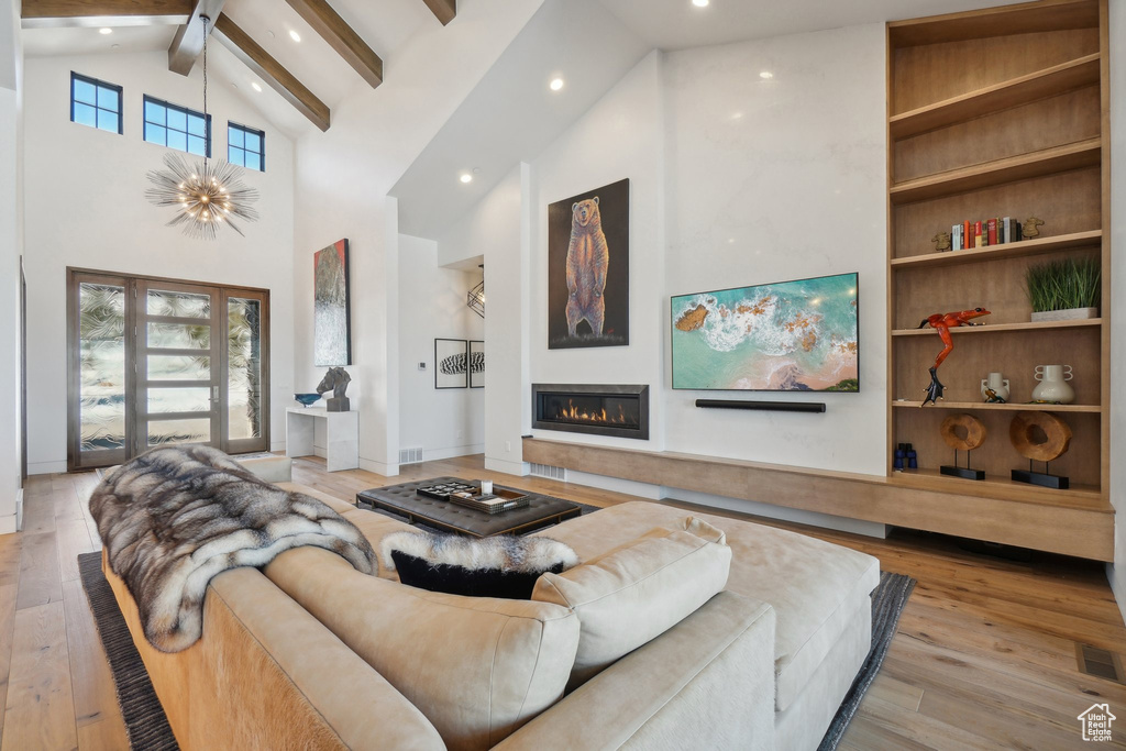 Living room with high vaulted ceiling, recessed lighting, beam ceiling, hardwood / wood-style floors, and a glass covered fireplace