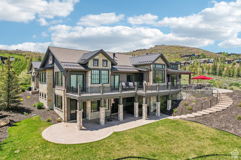 Back of house featuring stone siding, a standing seam roof, a patio, a lawn, and metal roof