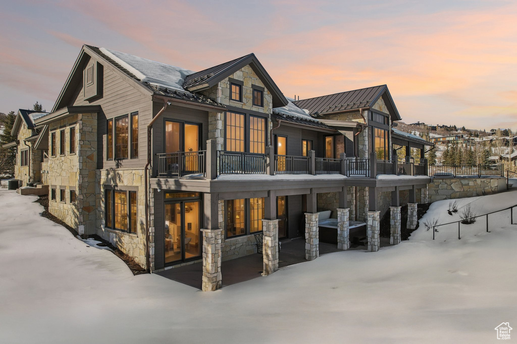 Snow covered house with stone siding, a standing seam roof, a balcony, and metal roof