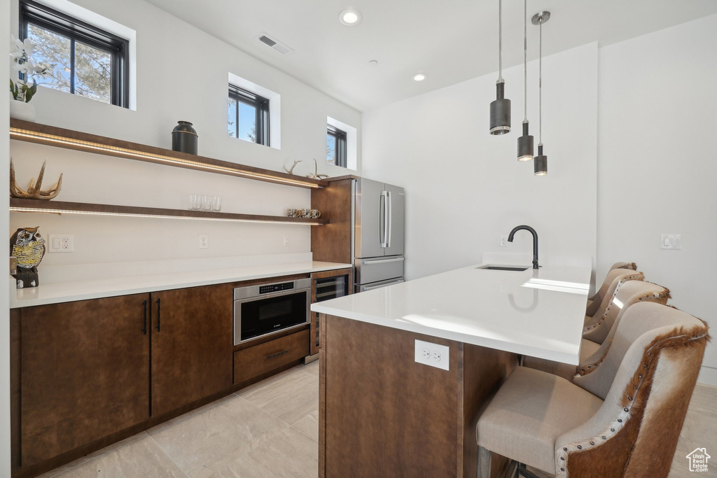 Kitchen featuring open shelves, a sink, freestanding refrigerator, a kitchen breakfast bar, and dark brown cabinets