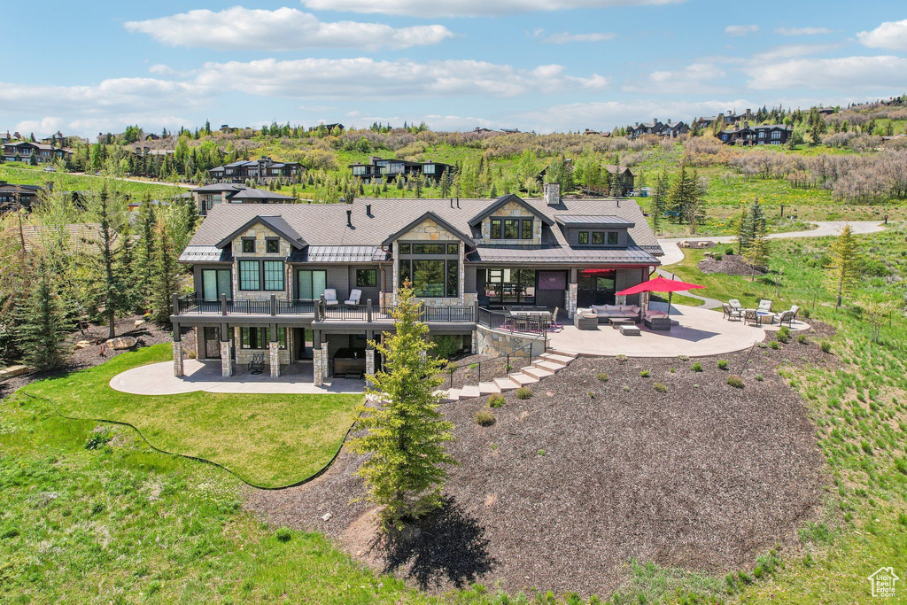 Rear view of house with a patio, stone siding, a chimney, and metal roof