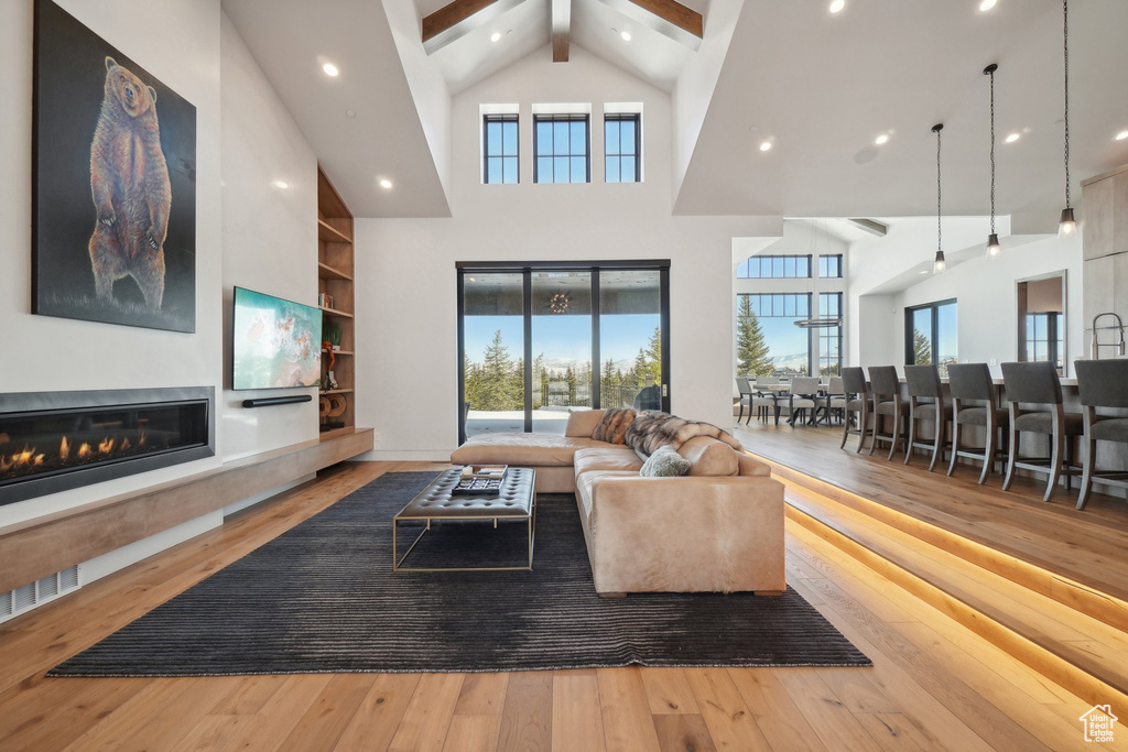 Living area with wood-type flooring, beam ceiling, high vaulted ceiling, a glass covered fireplace, and recessed lighting