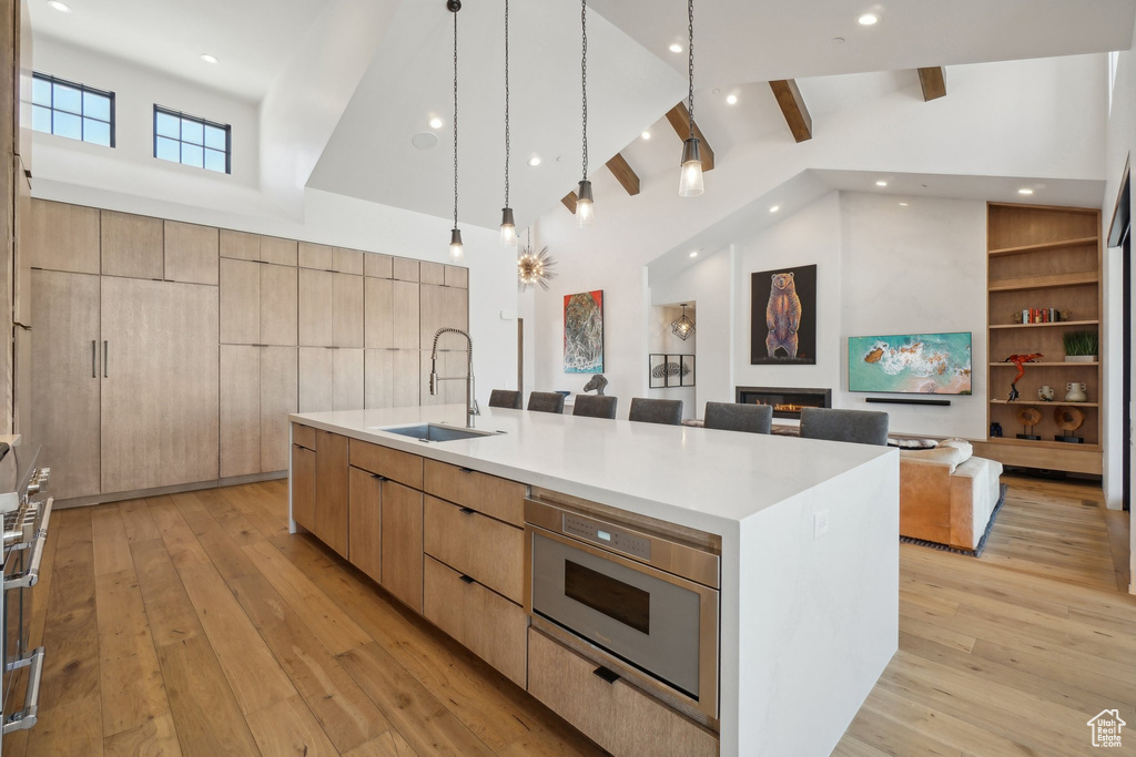 Kitchen featuring a sink, modern cabinets, open floor plan, light wood-style floors, and high vaulted ceiling
