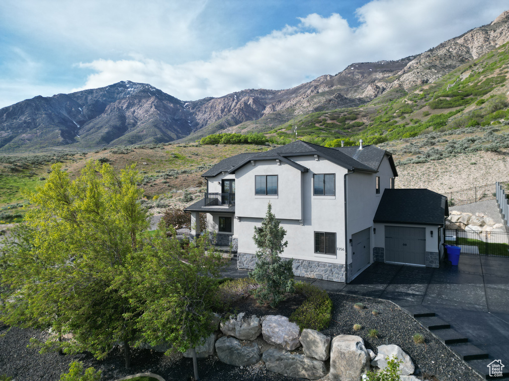 View of home\'s exterior featuring stone siding, a mountain view, an attached garage, a balcony, and driveway