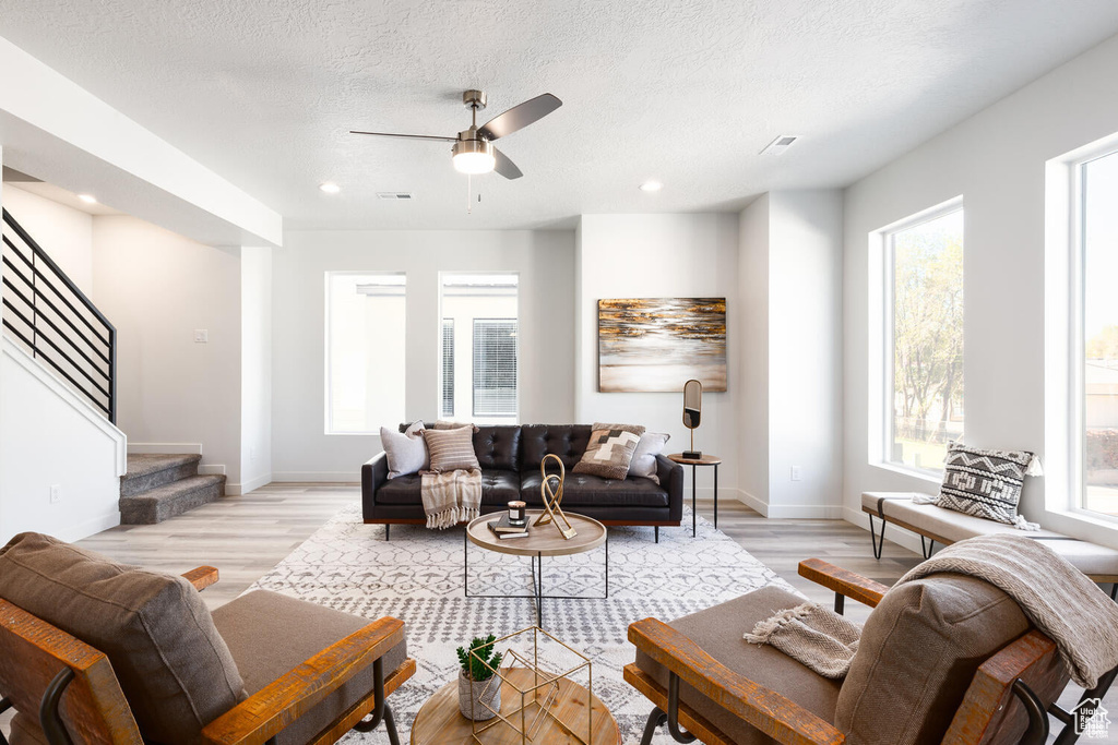 Living room with a textured ceiling, ceiling fan, light hardwood / wood-style floors, and plenty of natural light