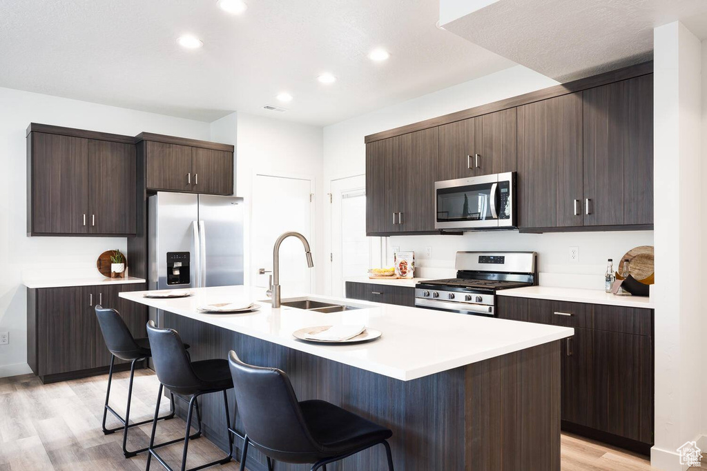 Kitchen with appliances with stainless steel finishes, a kitchen bar, light hardwood / wood-style flooring, and a kitchen island with sink