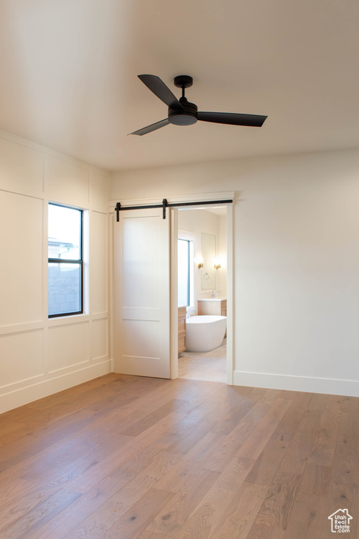 Unfurnished bedroom featuring ceiling fan, ensuite bath, a barn door, and hardwood / wood-style floors