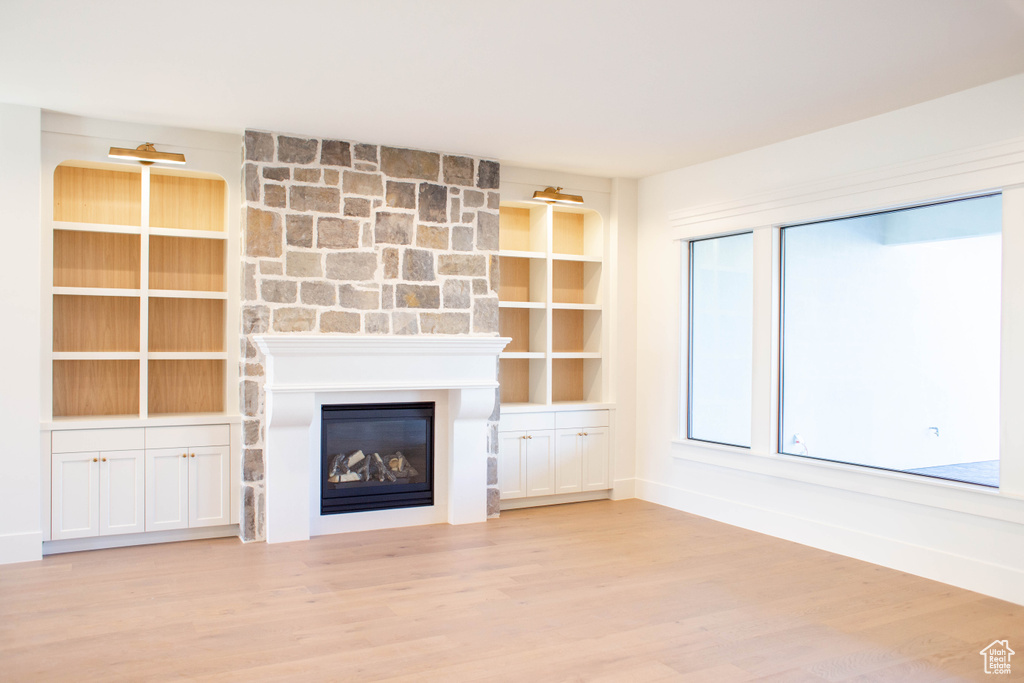 Unfurnished living room with a large fireplace, built in features, and light hardwood / wood-style floors