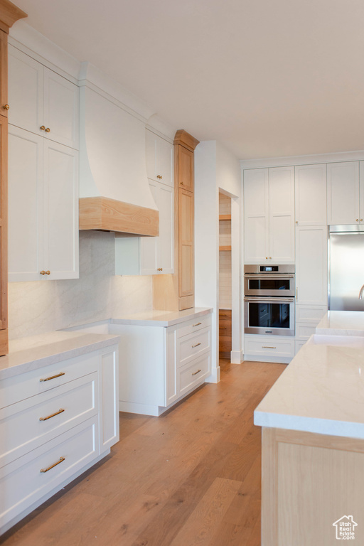 Kitchen featuring white cabinetry, stainless steel appliances, light hardwood / wood-style floors, and custom exhaust hood