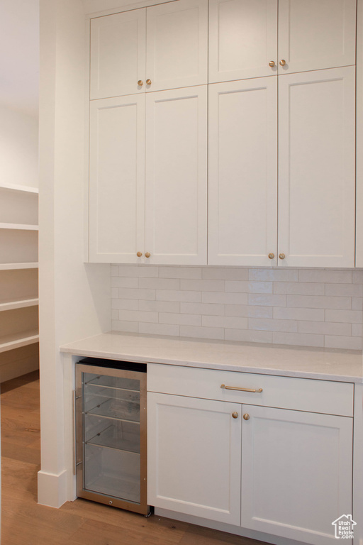 Bar featuring wine cooler, decorative backsplash, light hardwood / wood-style floors, and white cabinets