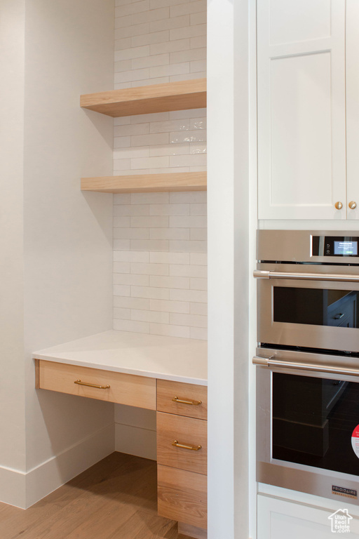 Kitchen with white cabinetry, double oven, and hardwood / wood-style floors