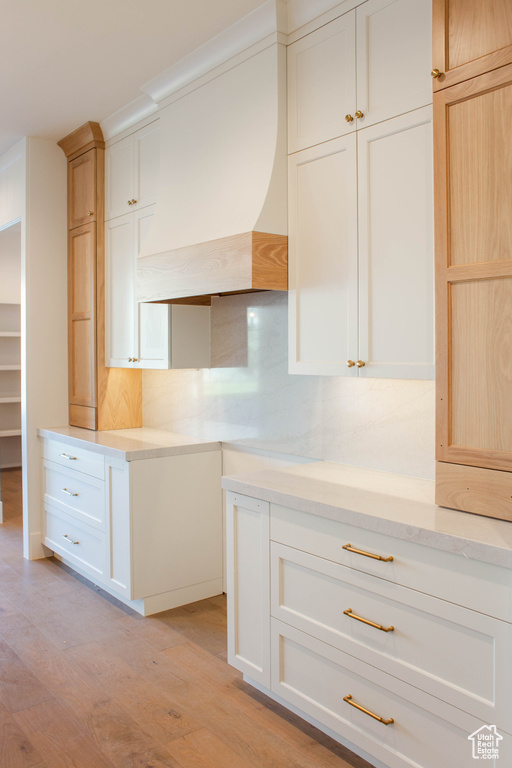 Kitchen with decorative backsplash, custom range hood, white cabinets, and light wood-type flooring