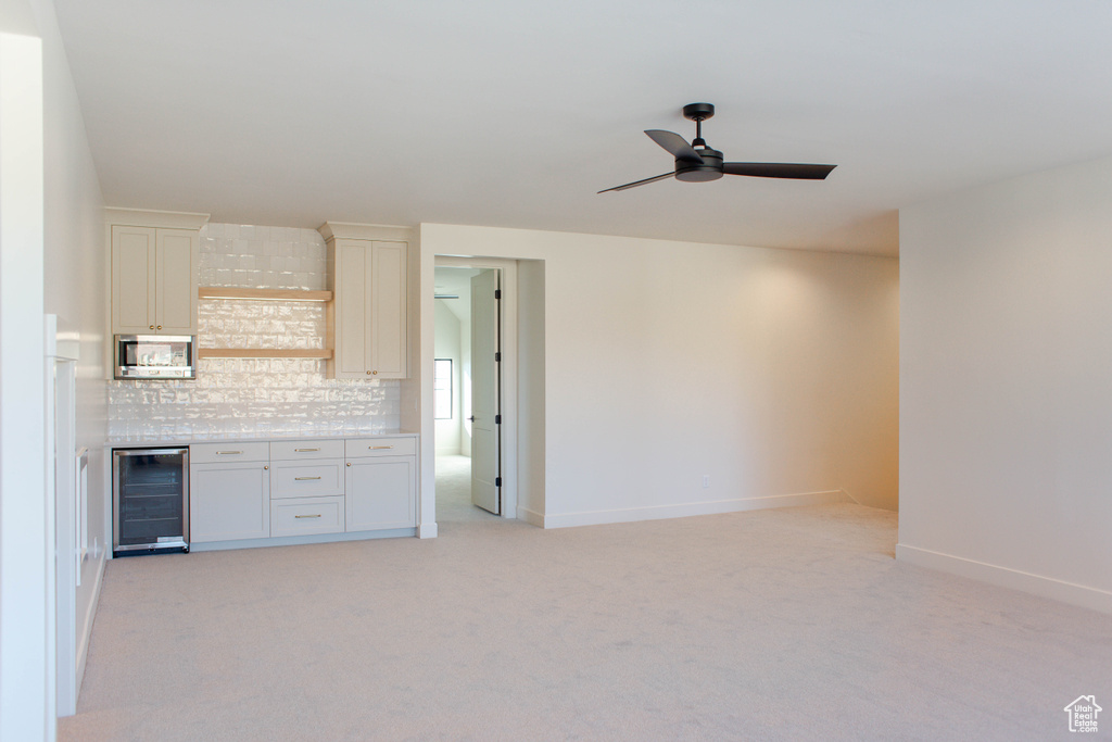 Kitchen with stainless steel microwave, tasteful backsplash, beverage cooler, light colored carpet, and ceiling fan