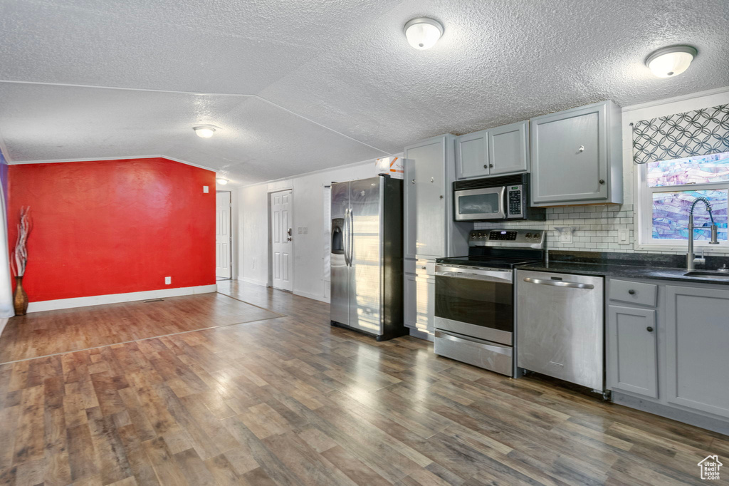 Kitchen with appliances with stainless steel finishes, lofted ceiling, sink, dark hardwood / wood-style floors, and gray cabinets