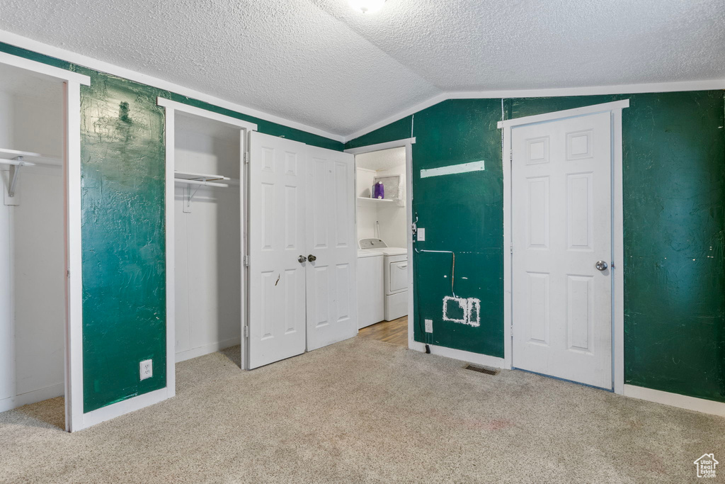 Unfurnished bedroom featuring a textured ceiling, lofted ceiling, washing machine and dryer, light colored carpet, and multiple closets