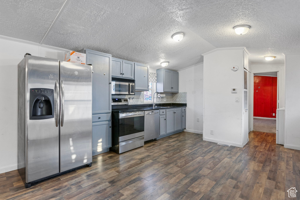 Kitchen featuring appliances with stainless steel finishes, gray cabinetry, dark hardwood / wood-style floors, backsplash, and lofted ceiling