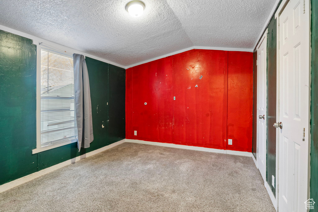 Carpeted spare room featuring a textured ceiling and vaulted ceiling