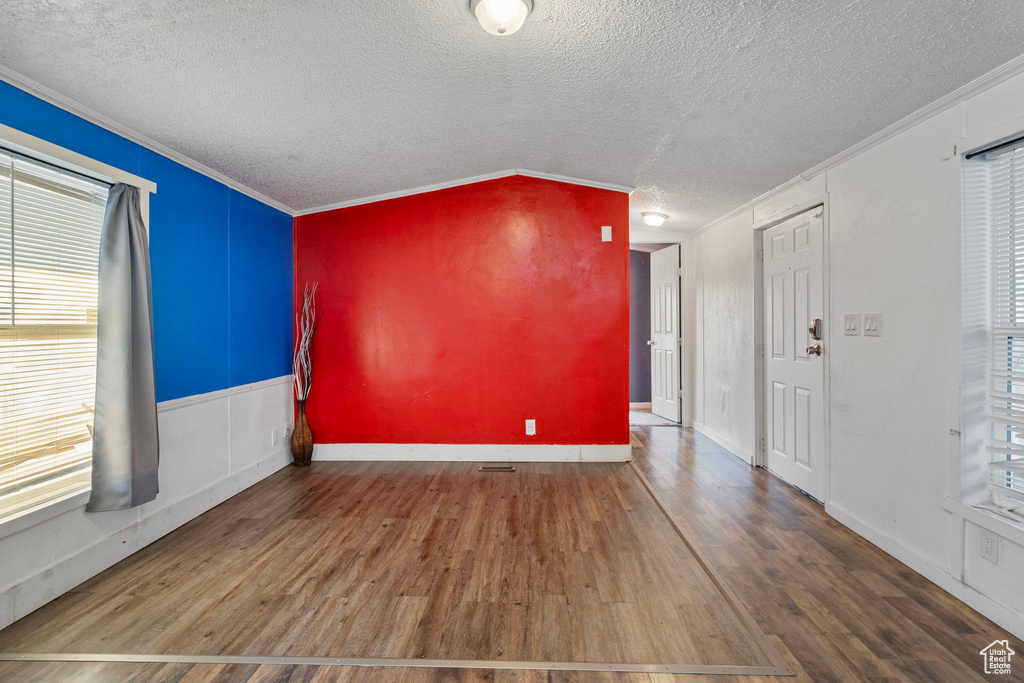 Empty room with hardwood / wood-style flooring, a textured ceiling, crown molding, and vaulted ceiling