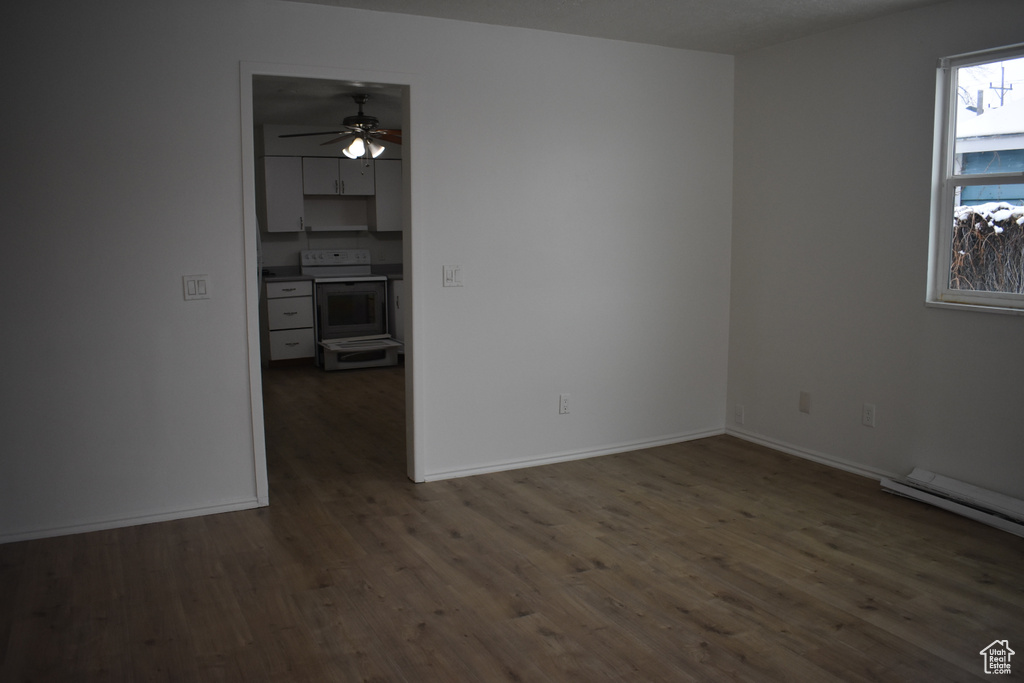Empty room featuring ceiling fan, a baseboard heating unit, and dark wood-type flooring
