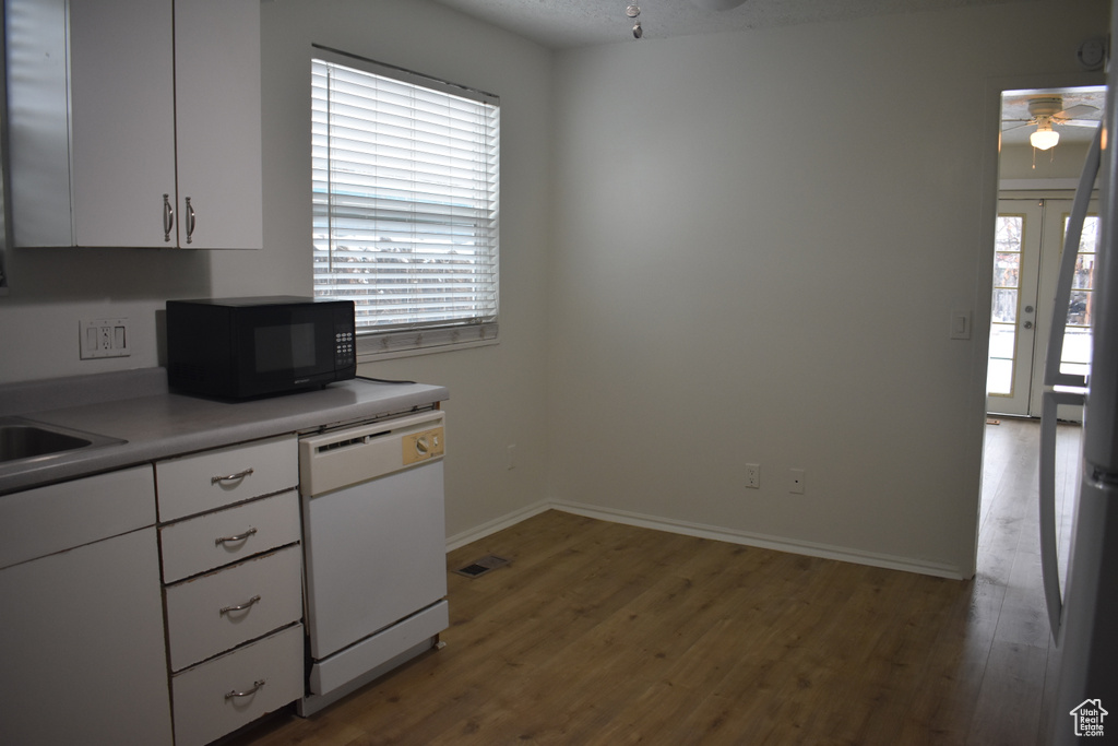 Kitchen with white dishwasher, hardwood / wood-style flooring, white cabinets, and ceiling fan