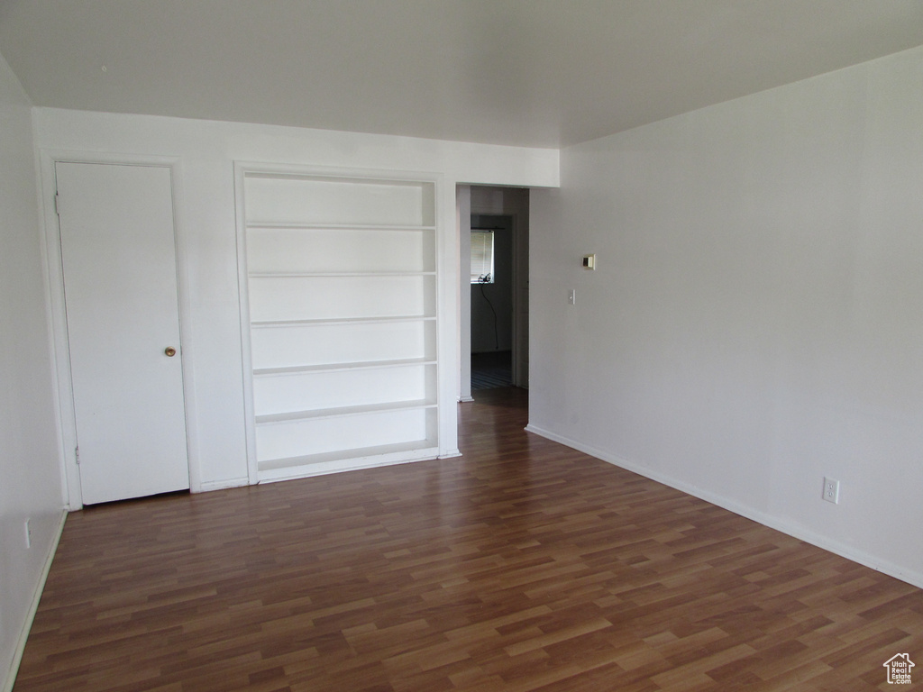 Empty room with dark wood-type flooring and built in shelves