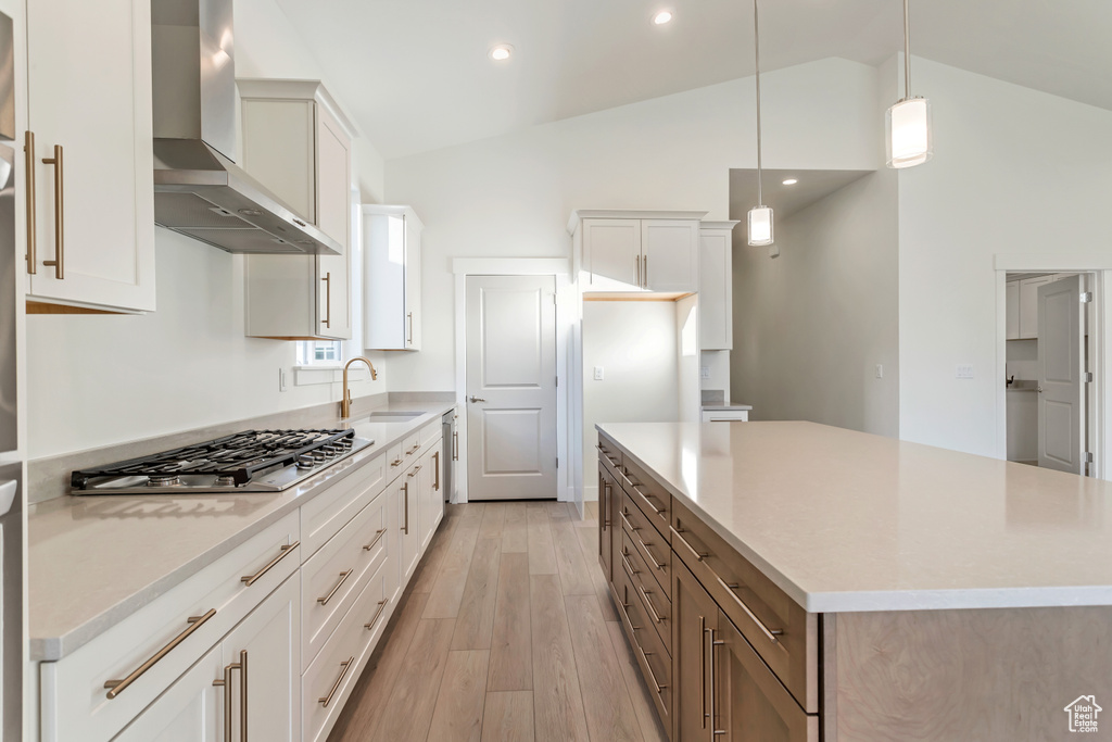 Kitchen featuring wall chimney exhaust hood, white cabinetry, a large island, vaulted ceiling, and stainless steel gas stovetop