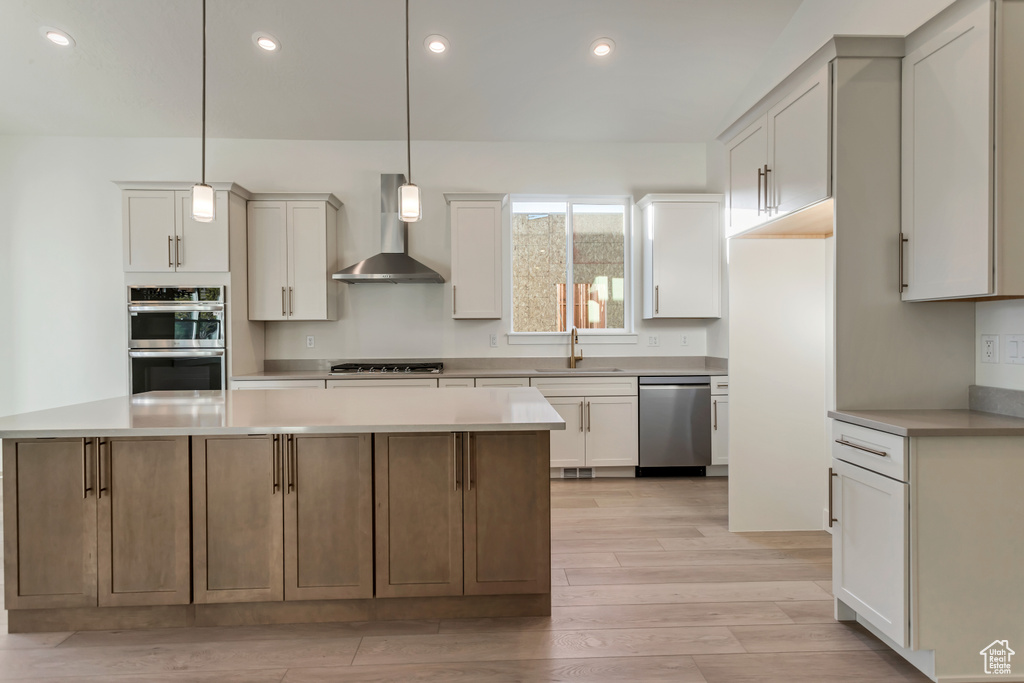 Kitchen with white cabinets, wall chimney range hood, appliances with stainless steel finishes, and sink