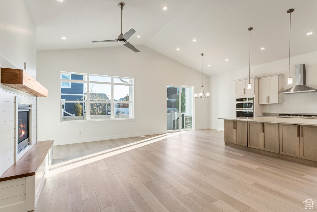 Kitchen with light hardwood / wood-style floors, gas stovetop, hanging light fixtures, wall chimney range hood, and ceiling fan with notable chandelier