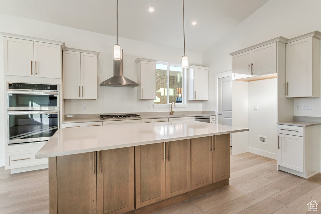 Kitchen with hanging light fixtures, wall chimney exhaust hood, white cabinetry, and a large island