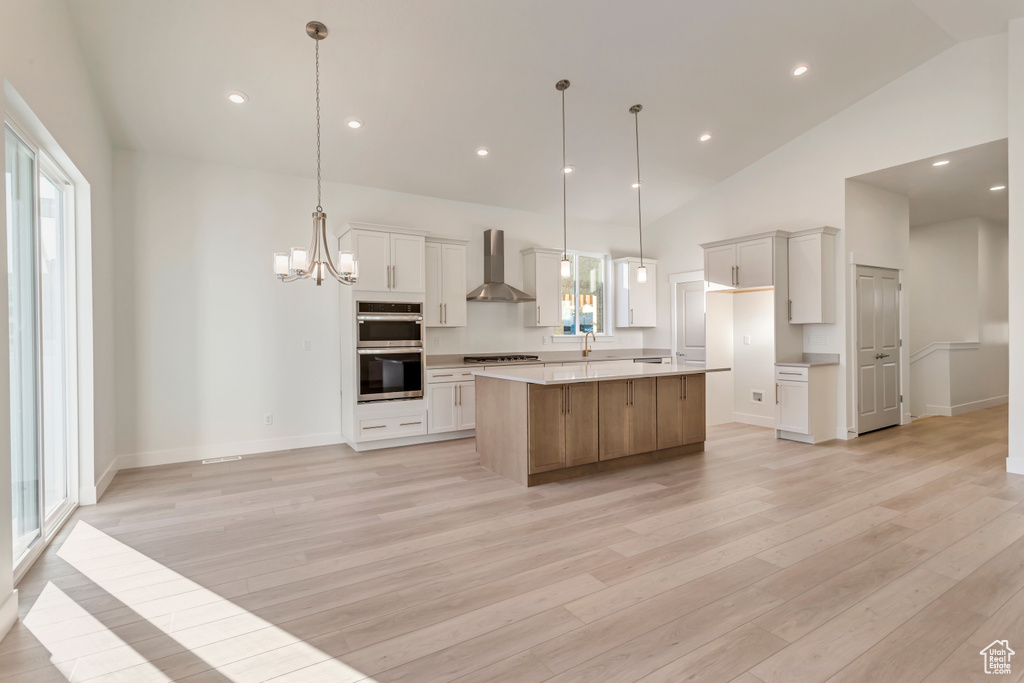 Kitchen featuring a large island, white cabinetry, wall chimney exhaust hood, and hanging light fixtures