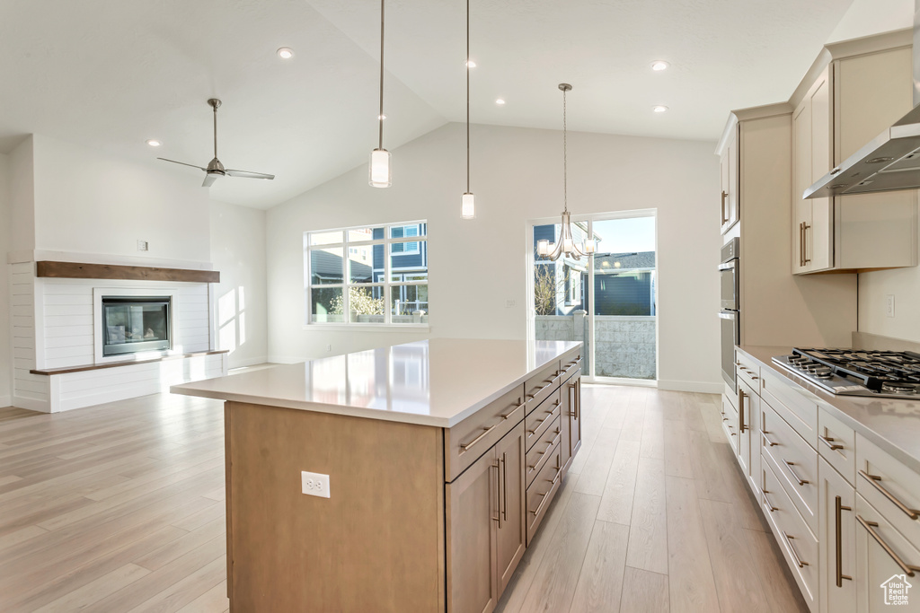 Kitchen with ceiling fan with notable chandelier, appliances with stainless steel finishes, decorative light fixtures, wall chimney range hood, and a large island