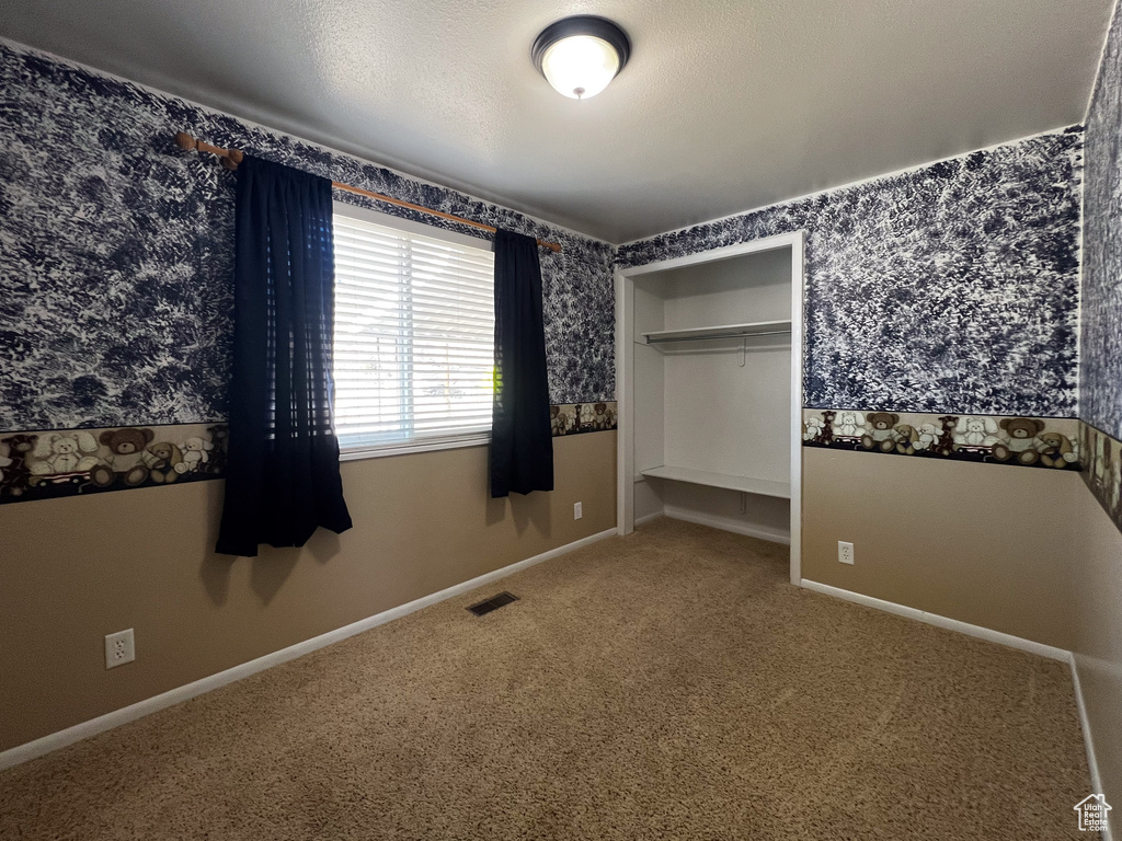 Unfurnished bedroom featuring carpet flooring, a textured ceiling, and a closet