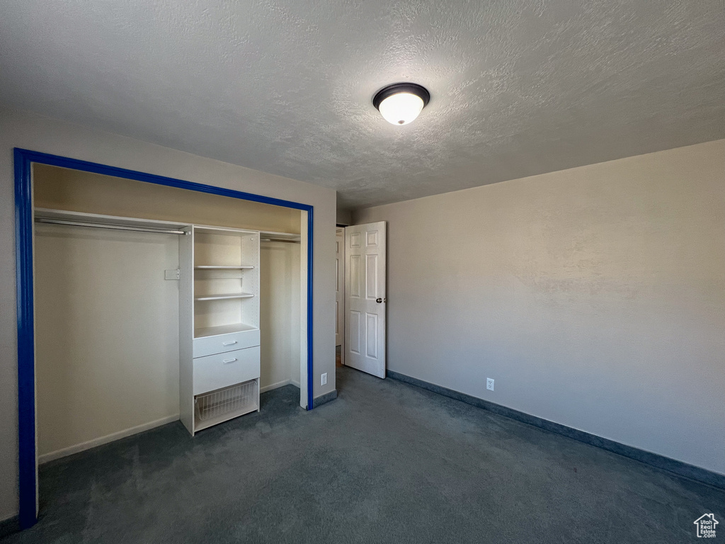 Unfurnished bedroom with dark carpet, a closet, and a textured ceiling