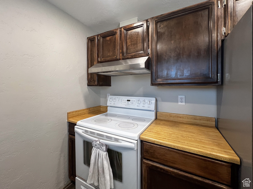 Kitchen with white range with electric cooktop, stainless steel fridge, and dark brown cabinets