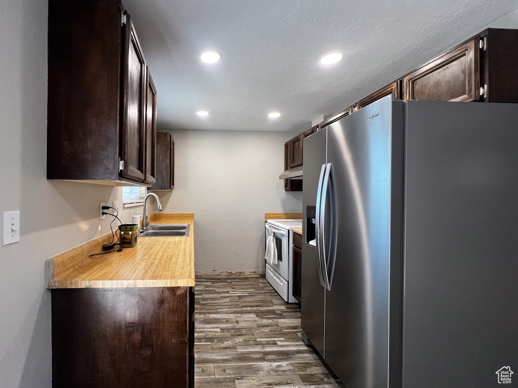 Kitchen featuring white electric range, sink, stainless steel fridge with ice dispenser, and dark brown cabinets