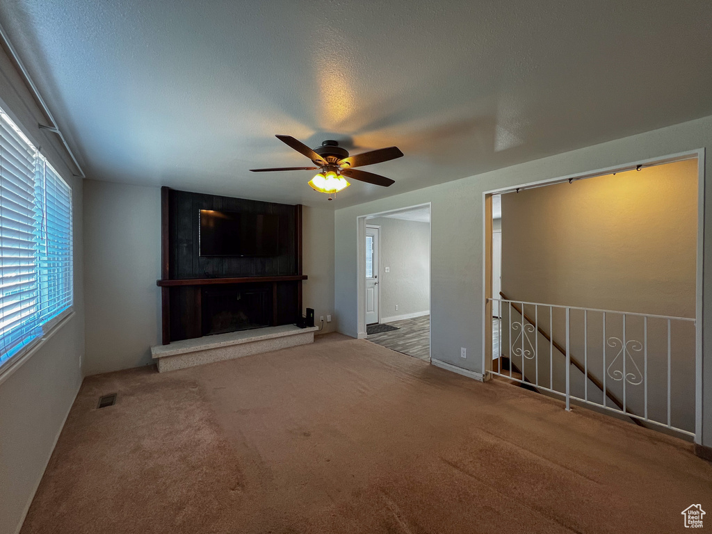 Unfurnished living room featuring a fireplace, ceiling fan, and carpet